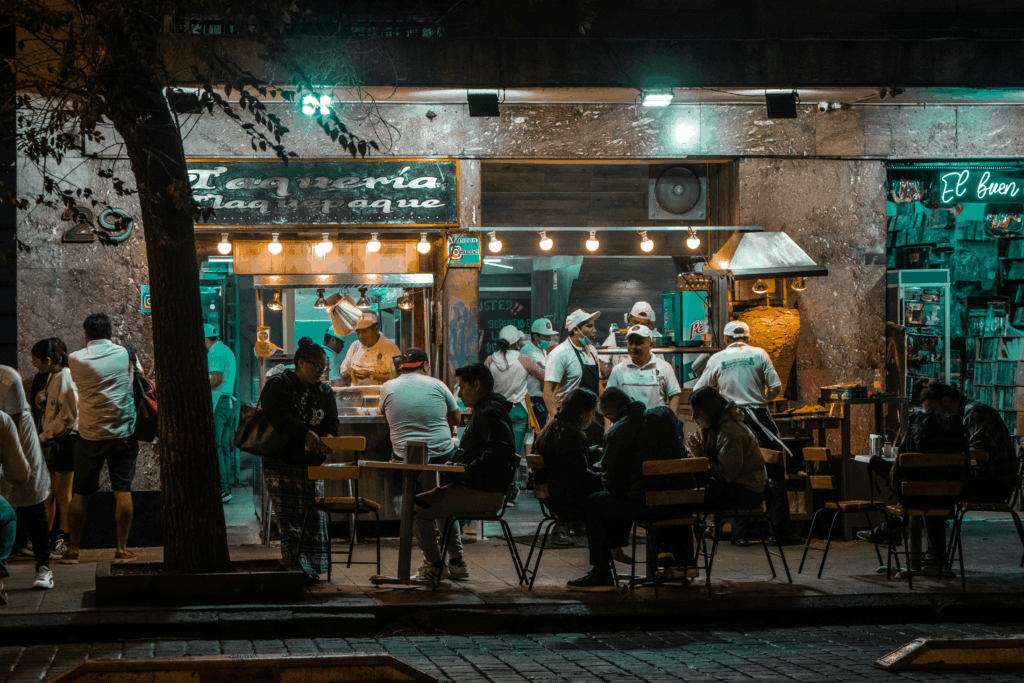 Lively outdoor restaurant in Mexico City at night, with diners enjoying food under glowing lights — capturing the vibrant culinary culture featured in food shows set in Mexico City.