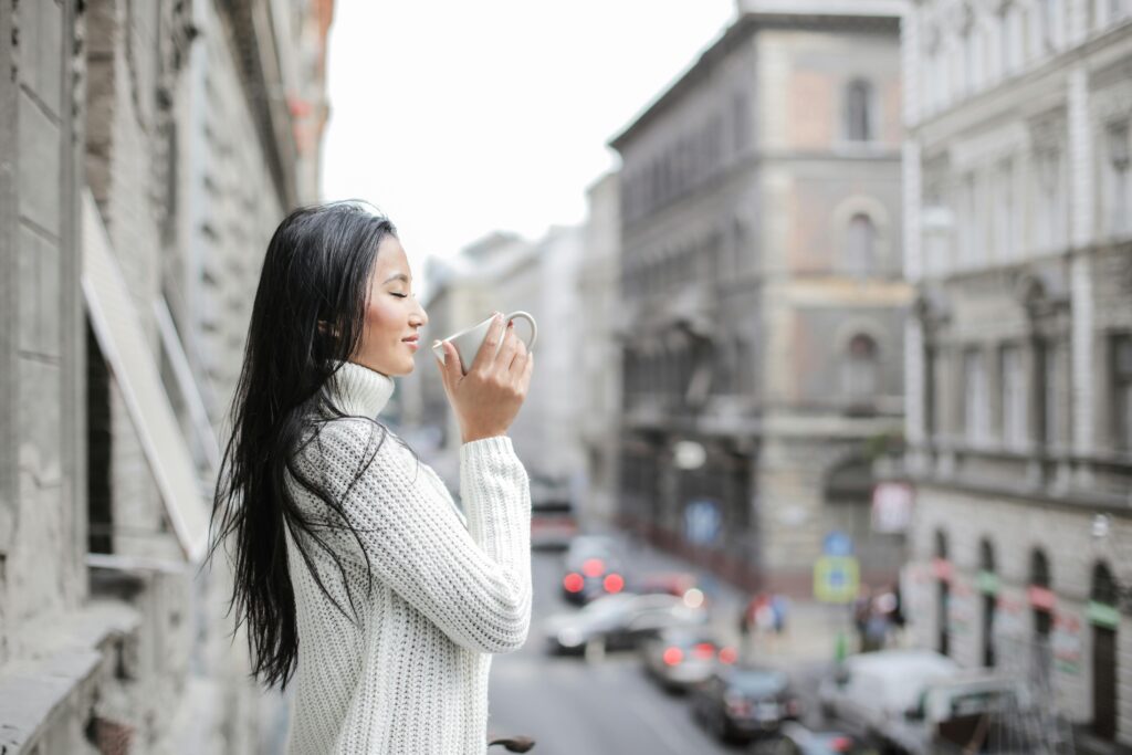 Elegant, fashion-forward woman sipping coffee on a sunlit balcony above a bustling Mexico City street.