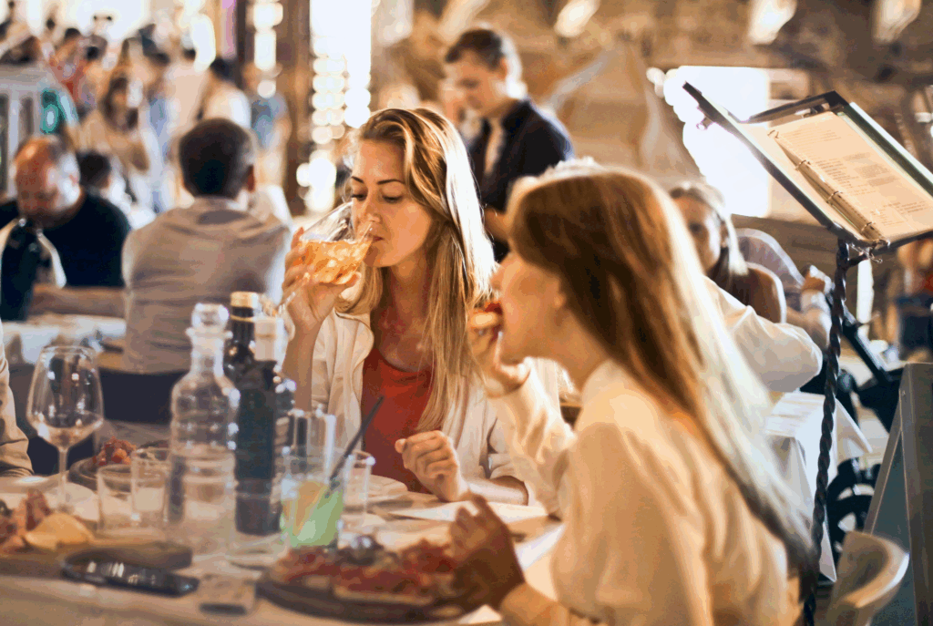 Two women enjoying food and wine in Tuscany — a lively scene that reflects the spirit of culinary films set in Tuscany and food travel shows.