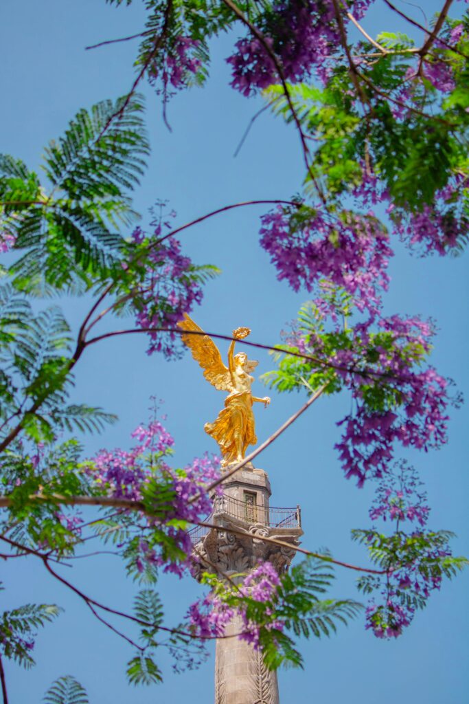 Close-up of Mexico City’s Independence Monument framed by purple flowers, a historic site often featured in personalized tours from Mexico City travel resources