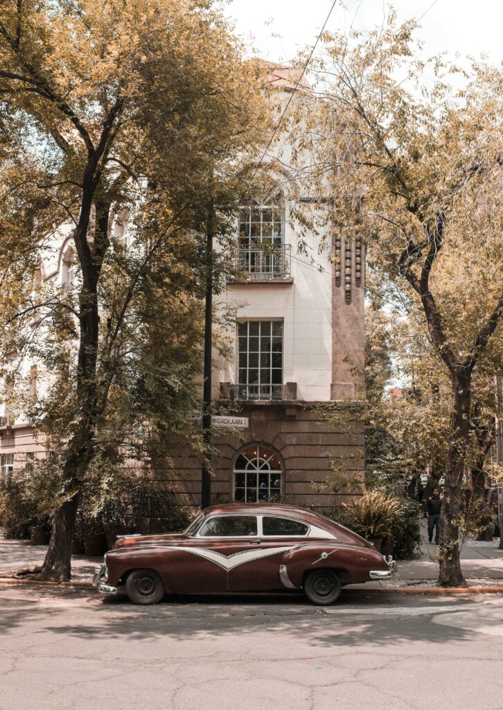 Tree-lined street in Mexico City with a vintage car parked in front of a brick home, a hidden gem you might discover through Mexico City travel podcasts and local tips